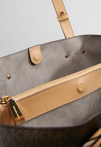 Interno di una borsa tote beige con una fodera in suede grigia, un compartimento con zip dotato di una cerniera dorata e una chiusura a scatto.