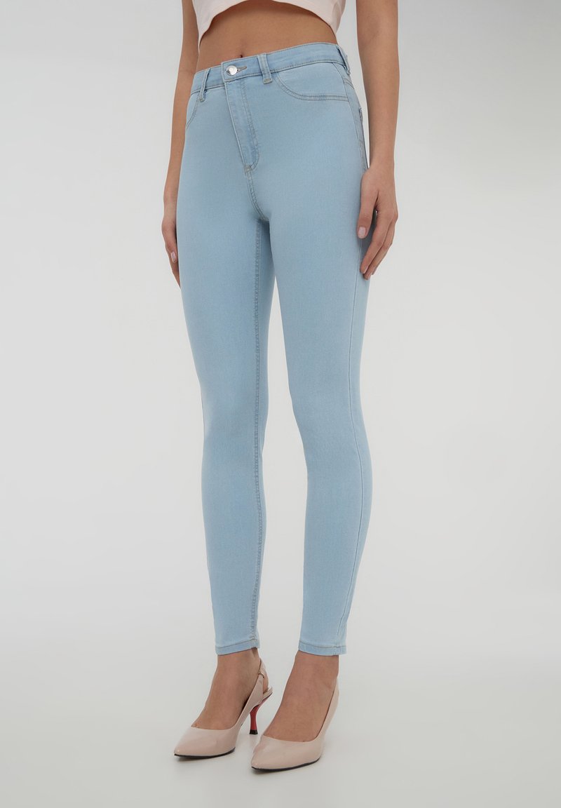 Jeans skinny blu chiaro con vita alta, dotati di chiusura con zip e bottone. Tessuto denim liscio, cuciture minime e senza decorazioni.