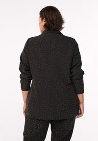 Schwarzer Blazer mit weißen Punkten, strukturierte Form, lange Ärmel und Reverskragen, von hinten betrachtet.