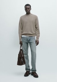 Maglione in lana beige sopra una maglietta bianca, jeans denim chiari, scarpe in pelle marrone e una borsa marrone. Texture liscia, vestibilità casual, design minimal.