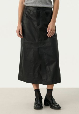 Schwarzer Leder-Midirock mit vorderer Naht und zwei Taschen. Er hat eine taillierte Taille und eine gerade Silhouette und wird mit schwarzen Loafers kombiniert.