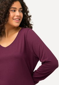 Halenka s dlouhým rukávem ve tmavě fialové barvě s výstřihem do V, vyrobená z hladkého, lehkého materiálu, s volným střihem a zakřiveným lemem.