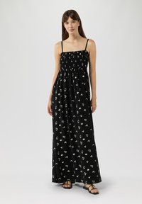 Zwarte maxidress met gesmockte bodice, dunne bandjes en witte abstracte patronen. Lichtgewicht stof, vloeiende silhouet en zijsplitten.