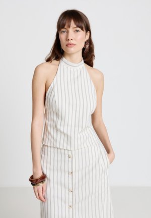 Femme portant un haut dos nu blanc sans manches et une jupe assortie à boutons avec des rayures verticales, accessoirisée avec des boucles d'oreilles et des bracelets.