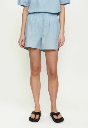 Osoba nosiaca svetlomodré šortky so sťahovacou šnúrkou, zladený top a čierne platformové sandále, stojaca na jednoduchom pozadí.