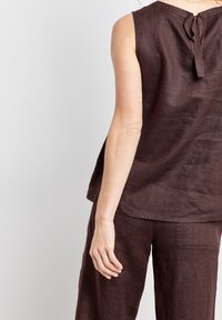 Top sin mangas de lino marrón con un detalle de lazo en la parte posterior, que cuenta con un corte relajado y una textura suave. Combinado con pantalones de lino marrón a juego.