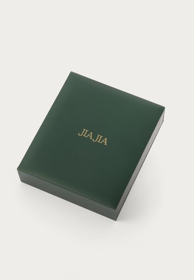 Zeleni kutija s glatkom površinom, s zlatnim natpisom "JLJIA" na vrhu. Dizajn je kvadratni s čistim rubovima i minimalnim detaljima.