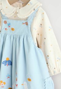 Vestido de pana azul claro con flores y abejas bordadas, botones de madera, cuello blanco con volantes y manga larga crema por debajo.