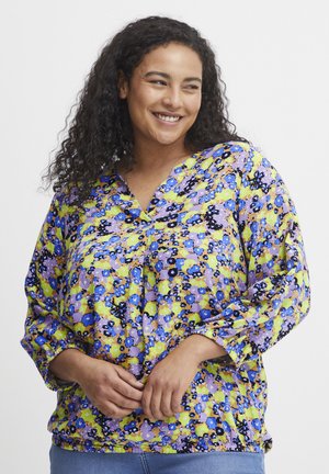 Blusa floral con escote en V y mangas largas. Presenta un patrón vibrante en amarillo, púrpura y azul, fabricada con un tejido ligero.