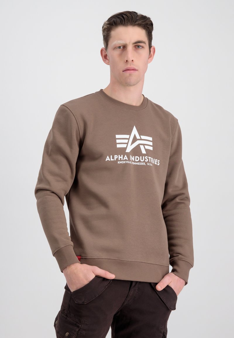 Sudadera marrón con cuello redondo, que presenta un estampado de logo blanco y puños acanalados sutiles. Tejido texturizado con un bolsillo lateral visible.