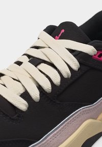 Μαύρο αθλητικό παπούτσι με μπεζ χοντρές κορδέλες, ροζ λογότυπο στη γλώσσα, ροζ λεπτομέρεια κοντά στις τρύπες των κορδονιών και λεπτομέριες στη σόλα σε μπεζ και μωβ.