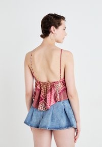 Top in tessuto rosa a pattern con spalline a spaghetti e orlo svasato, abbinato a una skort di jeans azzurri chiari con pieghe e orlo sfrangiato.
