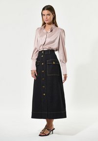Helles rosa Seidenhemd mit Rüscheneinsatz am Kragen, kombiniert mit einem dunklen Jeansrock mit goldenen Knöpfen und Taschen, abgerundet mit schwarzen High Heels.