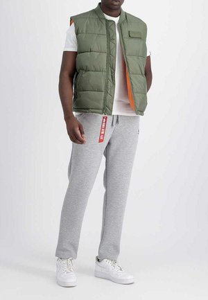 Green puffer vest with an orange interior, featuring a front pocket, paired with gray sweatpants and white sneakers. Includes a red tag detail.