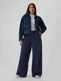 Jachetă din denim închis, cu o croială structurată și două buzunare frontale, asociată cu pantaloni din denim închis cu picior larg. Tricou alb dedesubt.