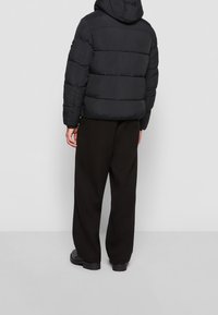 Czarna pikowana kurtka puchowa z kapturem, z przeszywanymi sekcjami. W zestawie z luźnymi czarnymi spodniami i solidnymi czarnymi butami.