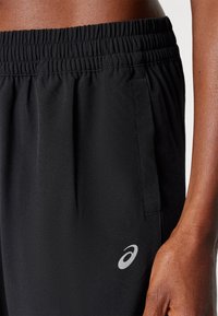 Svarta idrottsshorts med elastisk midja, sidofickor och en reflekterande logotyp på vänster sida. Slät, lättviktsmaterial.