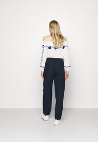 Biała bluzka bez ramiączek z niebieskim haftem w kwiaty, zestawiona z ciemnoniebieskimi spodniami i białymi trampkami. Prosty design i luźny krój.