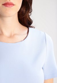 Jasnoniebieska, krótko rękawowa bluzka z okrągłym dekoltem i gładkim, miękkim materiałem. Prosty, minimalistyczny design bez widocznych wzorów czy ozdób.