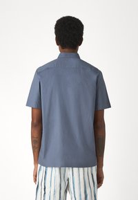 Kortärmad skjorta i enhetlig marinblå bomull, med standardkrage och rak nederkant, bärs tillsammans med randiga bomullsshorts.