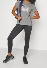 Grå t-shirt med rund hals och grafiskt tryck, tillsammans med mörkgrå leggings och svarta träningsskor. Inkluderar en lila ryggsäck.