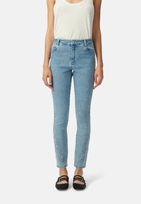 Jasnoniebieskie dżinsy o slim fit, z misternym niebieskim haftem przy dolnym brzegu, dopełnione białą bluzką na ramiączkach i czarnymi balerinami.