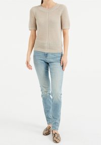 Beige stickad tröja med korta ärmar och strukturerad ribbstickning, kombinerad med ljusblå tajta jeans och ballerinaskor med ormmönster. Enkel och ren design.