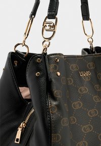 Borsa a mano in pelle nera con dettagli oro, dotata di chiusura a zip, logo e finitura testurizzata. Include accenti con motivo.