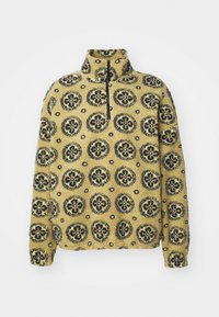 Pulover din fleece galben cu un design floral. Are un guler înalt și un fermoar la jumătate în față. Suprafață texturată cu accente de culoare albastru închis.