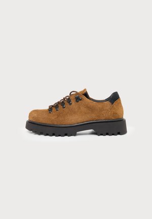 Chaussure à lacets en daim marron avec semelle noire épaisse et œillets métalliques, vue de côté sur un fond clair uni.