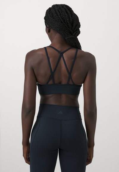 Μαύρο αθλητικό σουτιέν με σταυρωτά λουριά και λεία υφή, συνδυασμένο με ψηλόμεσα μαύρα κολάν που διαθέτουν διακριτική σήμανση.