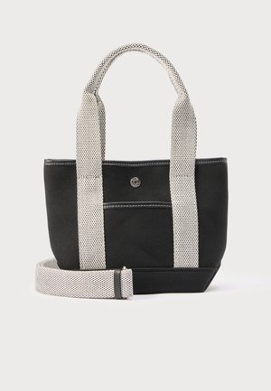 Zwarte canvas tas met brede witte hengsels en een afneembare lange riem, voorzien van een voorvak en een kleine ronde metalen knop.