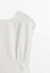 Blouse blanche avec un col arrondi, manches courtes, et un léger froncage sur les côtés. Tissu lisse avec une texture légère.