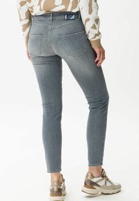 Vaqueros gris claro de corte ajustado con bolsillos traseros, combinados con zapatillas beige y blancas. La tela tiene una textura suave y un leve desvanecimiento.