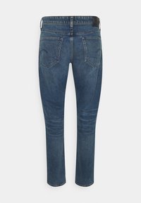 Tmavě modré denimové džíny s úzkým střihem, které mají pět kapes, vybledlé detaily a černou nášivku na pásu.