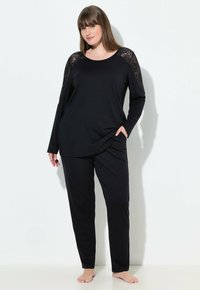 Conjunto de ropa de estar en negro que incluye una camiseta de manga larga con detalles de encaje en los hombros y pantalones de corte relajado. Material suave y caída ligera.