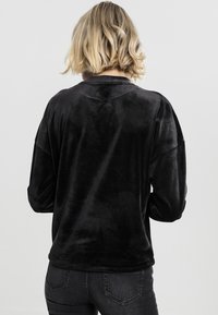 Sudadera de terciopelo negra con un ajuste holgado, hombros caídos y mangas largas. Textura suave y diseño simple y minimalista.