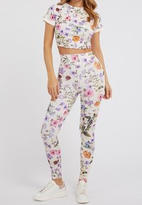 Bloemen crop top en legging set, witte stof met meerkleurige bloemenpatronen; aansluitend ontwerp, gecombineerd met witte sneakers voor een casual look.