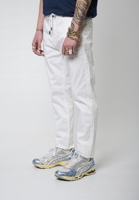 Pantalones de algodón blancos con un corte relajado, que cuentan con una cinturilla elástica. Combinados con zapatillas deportivas grises y plateadas con acentos azules.