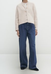 Helle rosa, texturierte Strickjacke mit rundem Ausschnitt und vier Knöpfen, kombiniert mit lockeren, dunkelblauen Jeans.