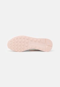 Light pink rubber sole of a Nike shoe with square-shaped traction studs and a textured heel on a white background.