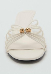 Sandale à lanières en matériau blanc doux avec deux perles dorées accentuées au centre et une semelle intérieure lisse et subtilement profilée.