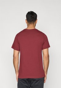 Μπλουζάκι από βαμβάκι σε μπορντό χρώμα με κοντά μανίκια, στρογγυλή λαιμόκοψη και λεία υφή, εμφανίζεται από πίσω. Μινιμαλιστικός σχεδιασμός.