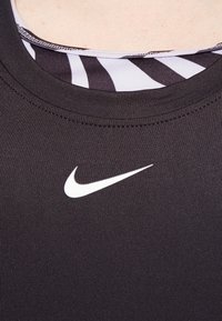 Zwarte athletische top met een geribbelde textuur en een wit Nike-logo op de voorkant. Bevat een gelaagde halslijn met daaronder een gestreept patroon.