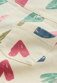 Bombažno blago s kremno ozadjem in pisanim vzorcem rdečih, zelenih, modrih in roza oblik. Vidni detajli šivov.