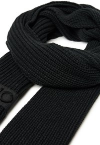 Sciarpa nera lavorata a maglia con un design a coste testurizzate, caratterizzata da un'etichetta nera elegante su un'estremità. Materiale morbido e forma versatile.