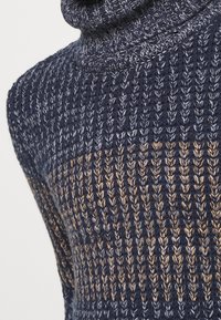 Pull en col montant tricoté avec une base bleu nuit foncé, un motif texturé et un dégradé d'accents brun clair.