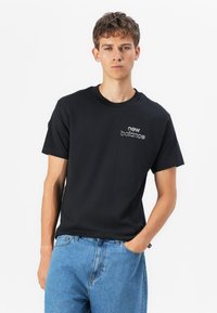 Black cotton t-shirt featuring a round neck, short sleeves, and a small embroidered "new balance" logo on the left chest.