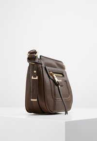 Ruskea nahkainen käsilaukku, jossa on kuoremainen pinta, kullanväriset metalliosat ja etutasku vetoketjulla. Varustettu säädettävällä olkahihnalla.