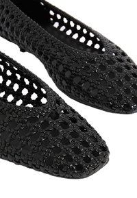 Ballerine nere con un intricato motivo intrecciato, dotate di punta affusolata e lati aperti. Realizzate in materiale flessibile, con una finitura liscia.